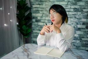 portrait de Jeune femme en pensant tandis que sérieux travail à Accueil avec portable sur bureau photo