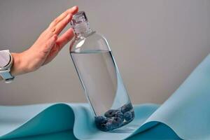 une femme main atteint pour une verre bouteille de l'eau avec myrtilles. photo