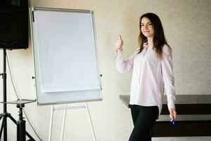 Jeune caucasien orateur femme entraîneur spectacle sur blanc conseil, pouce en haut signe. femelle équipe chef approuver projet idées. photo