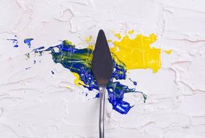 Un couteau à palette de peinture isolé sur un fond peint en blanc peinture d'un bleu et jaune avec copie espace