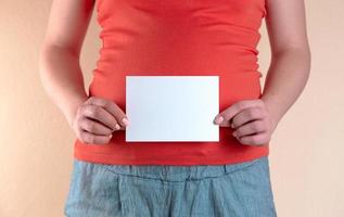 Une vue rapprochée du ventre d'une femme enceinte qui tient une feuille de papier vide photo