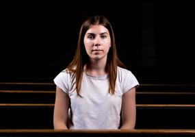 une jeune fille est assise seule dans une grande salle en regardant la caméra photo