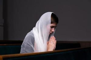 une jeune fille modeste avec un mouchoir sur la tête est assise à l'église et prie