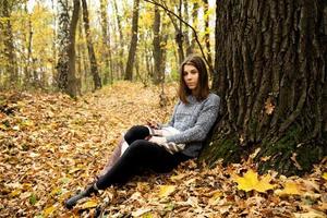 Belle jeune fille dans une veste grise assise dans la forêt d'automne photo