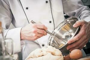 chef fouetter Battre et en train de préparer pâte dans cuisine. photo