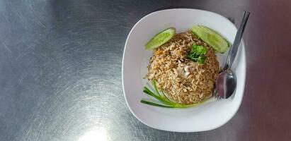 Haut vue ou plat allonger de Crabe Viande frit riz avec tranches concombre, coriandre, printemps oignon ou Scallion et cuillère avec fourchette dans blanc plat sur inoxydable acier table ou Contexte avec la gauche copie espace photo