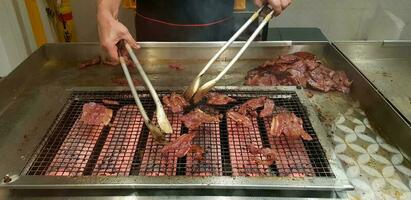 proche en haut beaucoup grillé rouge porc ou barbecue nourriture sur le net le fourneau avec mouvement de du chef main en utilisant ustensile dans le cuisine à Singapour. sélectif concentrer et délicieux concept photo