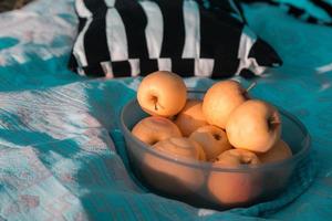 Assiette avec pommes jaunes sur un couvre-lit bleu sur une journée ensoleillée photo