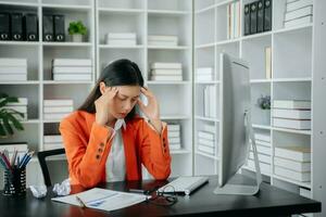 asiatique femme sentiment migraine tête souche.surmené femme d'affaires financier tandis que travail sur portable et tablette à bureau. photo