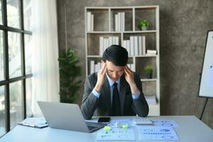 jeune homme d'affaires frustré travaillant sur un ordinateur portable assis sur son lieu de travail au bureau photo