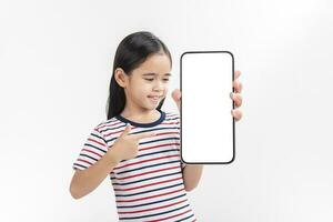 asiatique peu fille en portant téléphone intelligent maquette de Vide écran et souriant sur blanc Contexte. photo