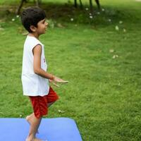 asiatique intelligent enfant Faire yoga pose dans le société parc Extérieur, enfants yoga pose. le peu garçon Faire yoga et méditation exercer. photo