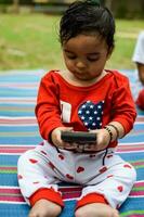 mignonne peu Indien bébé séance profiter Extérieur tirer à société parc dans Delhi, mignonne bébé garçon séance sur coloré tapis avec herbe autour, bébé garçon Extérieur tirer photo