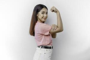 excité asiatique femme portant une rose T-shirt montrant fort geste par levage sa bras et muscles souriant fièrement photo