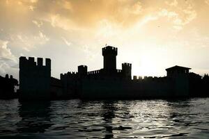 italie - silhouette du château de sirmone sur le lac de garde au coucher du soleil. architecture médiévale avec tour. photo