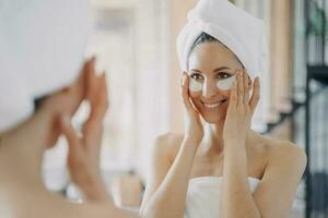jolie femme latina avec des patchs sous les yeux regardant un miroir pendant le traitement quotidien des soins de la peau photo