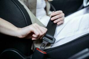 tondu vue de femme fixation sécurité ceinture tandis que séance dans voiture sur flou premier plan. Couper vue de Jeune femme mains verrouillage siège ceinture dans auto. séance seule. proche en haut photo