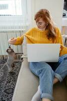 Jeune magnifique femme Faire en ligne travail à maison, magnifique sphynx chat distrayant propriétaire de travail photo