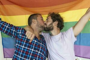 deux Jeune gay les amoureux embrasser chaque autre affectueusement. deux Jeune Masculin les amoureux permanent ensemble contre une fierté drapeau. affectueux Jeune gay couple partage une romantique moment ensemble. photo