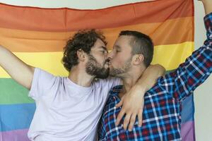 deux Jeune gay les amoureux embrasser chaque autre affectueusement. deux Jeune Masculin les amoureux permanent ensemble contre une fierté drapeau. affectueux Jeune gay couple partage une romantique moment ensemble. photo