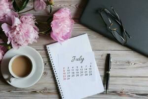 juillet calendrier, une bouquet de pivoines et une tasse de café photo