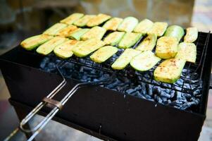 fermer de Zucchini tranches, étant mariné et cuit plus de flamboyant charbon barbecue gril dans le cour. un barbecue fête photo