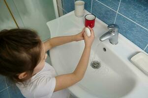 mains hygiène et virus les infections la prévention. aérien vue de peu fille la lessive mains avec savon bar à Accueil salle de bains photo