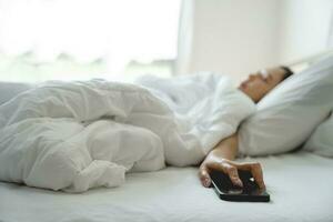 magnifique asiatique fille en train de dormir sur blanc lit. elle est tombée endormi avec sa téléphone intelligent dans main. photo