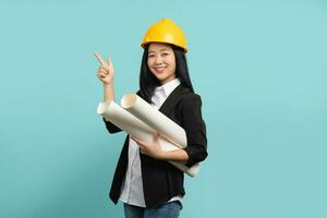 souriant professionnel asiatique femelle architecte, ingénieur dans sécurité casque présenter construction projet, montrer du doigt main et porter plan photo