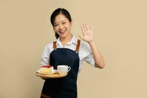 Jeune asiatique serveuse barista dans blanc chemise et tablier main tenir café boisson sur en bois plateau souriant chaud, Bienvenue inviter client à sa café magasin photo