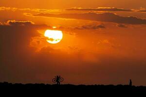 silhouette de une homme et le sien vélo à une magnifique le coucher du soleil suivant à le mer photo