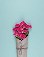 Bouquet de petites roses roses à fleurs enveloppées de papier kraft sur fond bleu photo