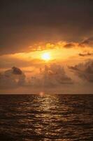 brillant ardent coloré mer le coucher du soleil - nuageux ciel et ondulations sur le l'eau - verticale magnifique paysage à le coucher du soleil dans Jaune rouge et Orange couleurs photo