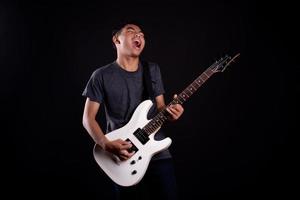 Jeune homme en veste de cuir noir avec guitare électrique sur fond noir en studio photo