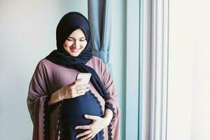 Jeune Enceinte arabe femme dans hijab en utilisant sa mobile téléphone à envoyer message photo