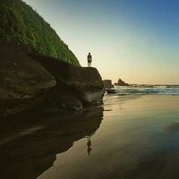 silhouette de une gars sur une rive dans bali à le coucher du soleil photo