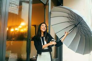 une magnifique Jeune content professionnel Indien femme portant formels en riant avec une téléphone et ouvert parapluie dans sa mains photo