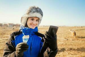 Jeune souriant caucasien femme à la recherche à le sien téléphone portant hiver vêtements photo