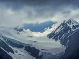 doux se concentrer. magnifique minimaliste paysage avec gros neigeux Montagne pics au dessus faible des nuages. atmosphérique minimalisme avec grand neige Montagne hauts, foncé glacier dans nuageux ciel. photo