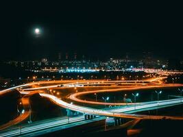 une nuit route jonction dans un industriel zone de une moderne métropole. aérien voir. longue obturateur la vitesse avec flou lumières de le phares photo