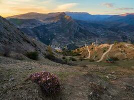 authentique ville en dessous de le Roche avec serpentin saleté route. ancien daghestanais Montagne village de gunib dans lever du soleil. Russie. photo