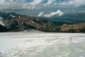 atmosphérique alpin vue à ramolli neige Montagne intervalle avec faible des nuages. scénique paysage avec magnifique neige montagnes dans faible des nuages. chaud temps sur le glacier, global chauffage concept. photo