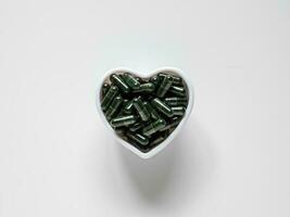 vert chlorella pilules. spiruline capsules dans bol sur blanc Contexte. Haut voir. photo