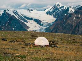 solo randonnée. camping sur une rocheux haute altitude plateau. blanc tente sur le Contexte de glacier et haute enneigé montagnes. photo