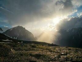 spectaculaire paysage avec le brillant des rayons de le Soleil par le des nuages plus de le montagnes. brillant dernier des rayons de le réglage Soleil plus de une montagneux désert plateau. photo