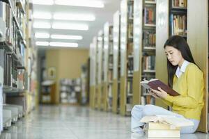 étudiant séance sur le sol et en train de lire à bibliothèque. photo