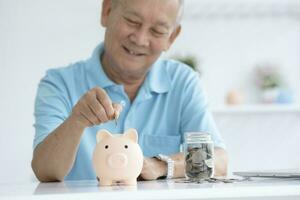 aîné homme souriant en mettant une pièce de monnaie à l'intérieur porcin banque. photo