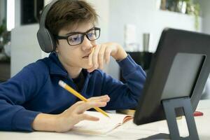 Jeune garçon en utilisant ordinateur et mobile dispositif en train d'étudier en ligne. photo