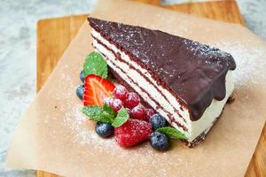 une tranche de gâteau au chocolat décoré de fruits rouges sur une planche de bois