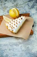 un morceau de tarte au citron décoré d'une tranche de citron sur une planche de bois